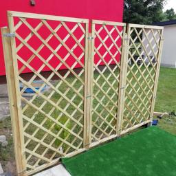 Rafi-Potrafi - Drewniana, ażurowa osłona tarasowa z trzema segmentami, zamontowana na zewnątrz, z widoczną czerwoną ścianą budynku w tle i fragmentem sztucznej trawy na podłożu.