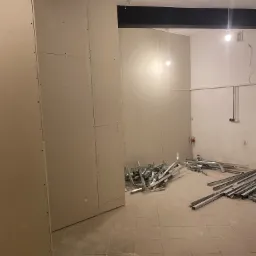 Montaż płyt karton-gips na ścianach z widocznymi profilami metalowymi na podłodze, surowy stan wykończenia wnętrza.