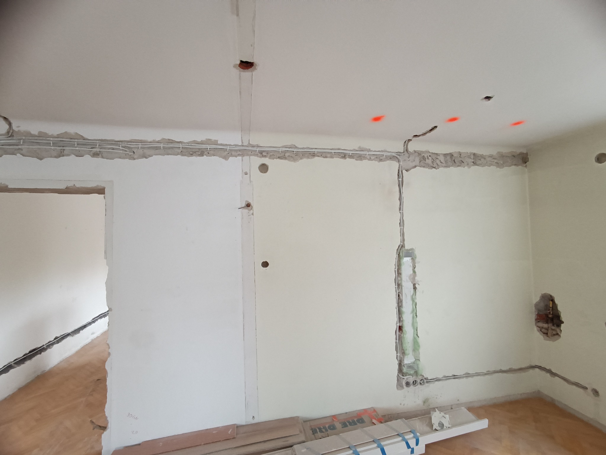 Wnętrze w trakcie remontu z widocznymi przewodami elektrycznymi ułożonymi wzdłuż ścian i sufitu, przygotowane do tynkowania. Widoczne puszki instalacyjne.