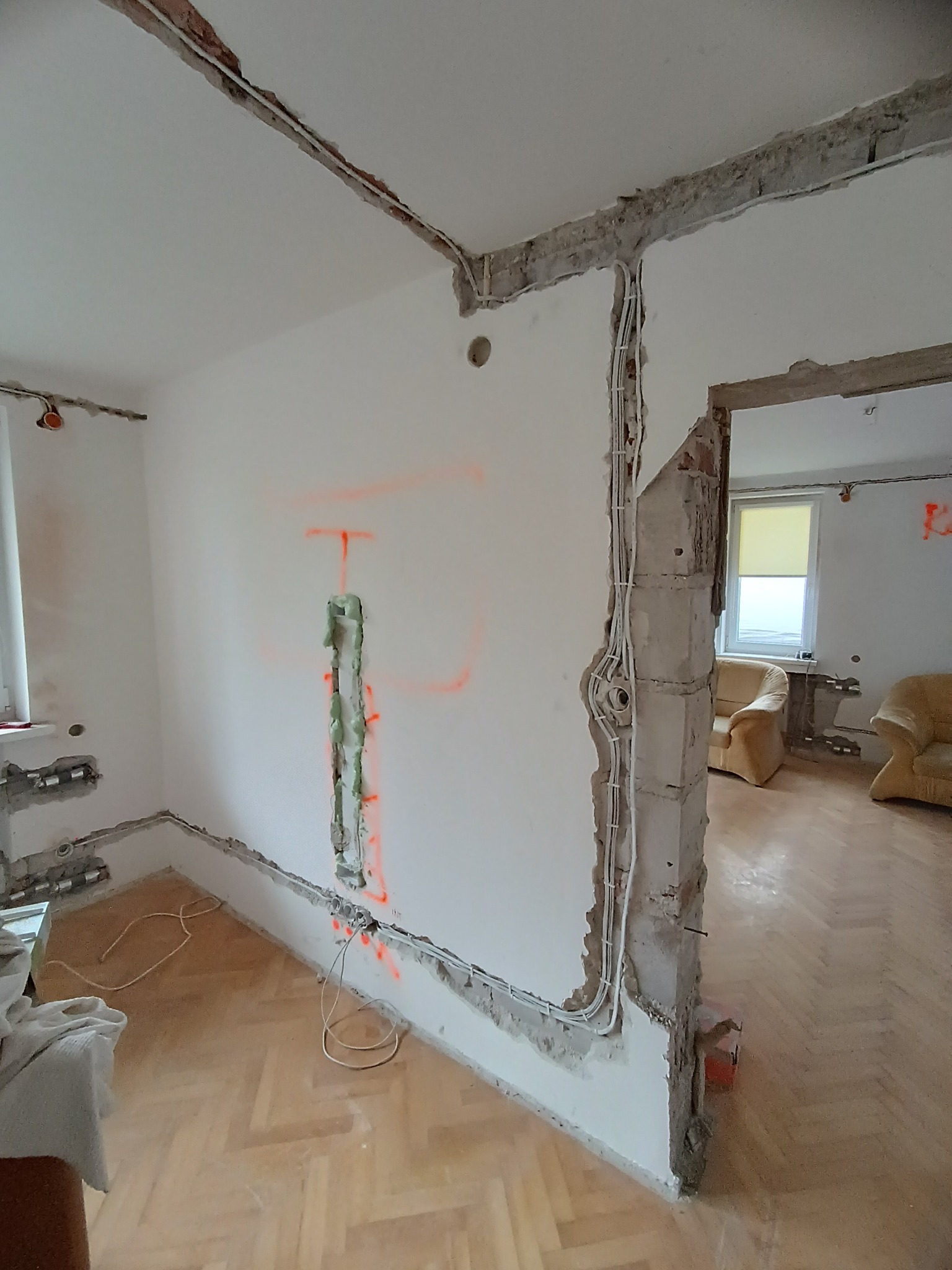 Wnętrze w trakcie remontu: bruzdy w ścianach pod kable, widoczne przewody elektryczne, ślady po kuciu, parkiet. Prace przygotowawcze do instalacji elektrycznej.