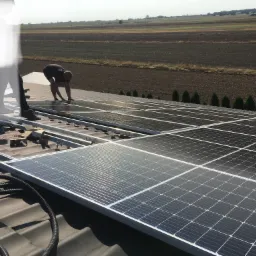 Montaż paneli fotowoltaicznych na dachu z widocznym krajobrazem pól uprawnych w tle.