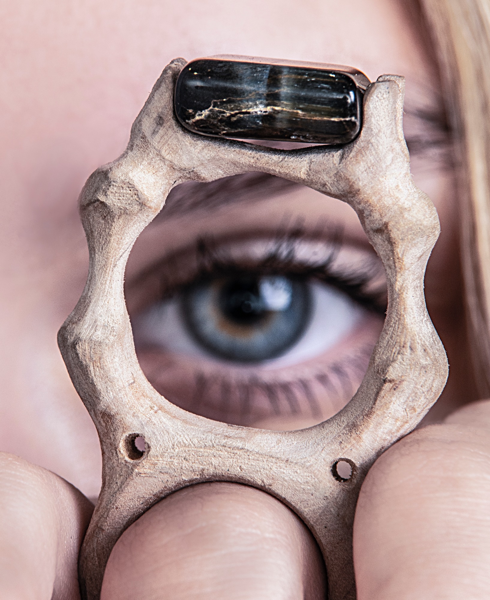 Oko kobiety spoglądające przez drewniany pierścień z czarnym kamieniem, makro.