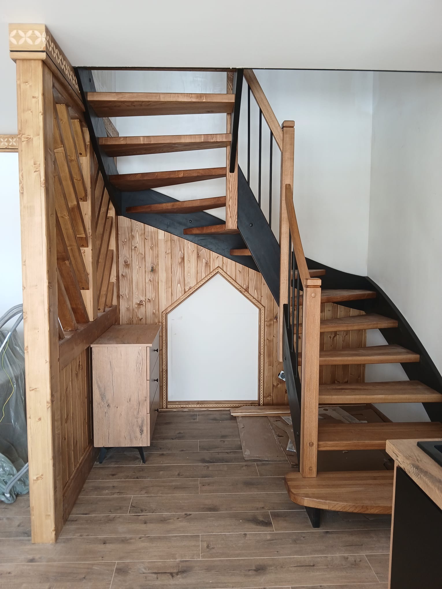 Dwubiegowe schody z drewna i metalu z Zakopanego, z dekoracyjnym wykończeniem i szafką pod spodem. Widok z dołu, ukazujący detale konstrukcji.