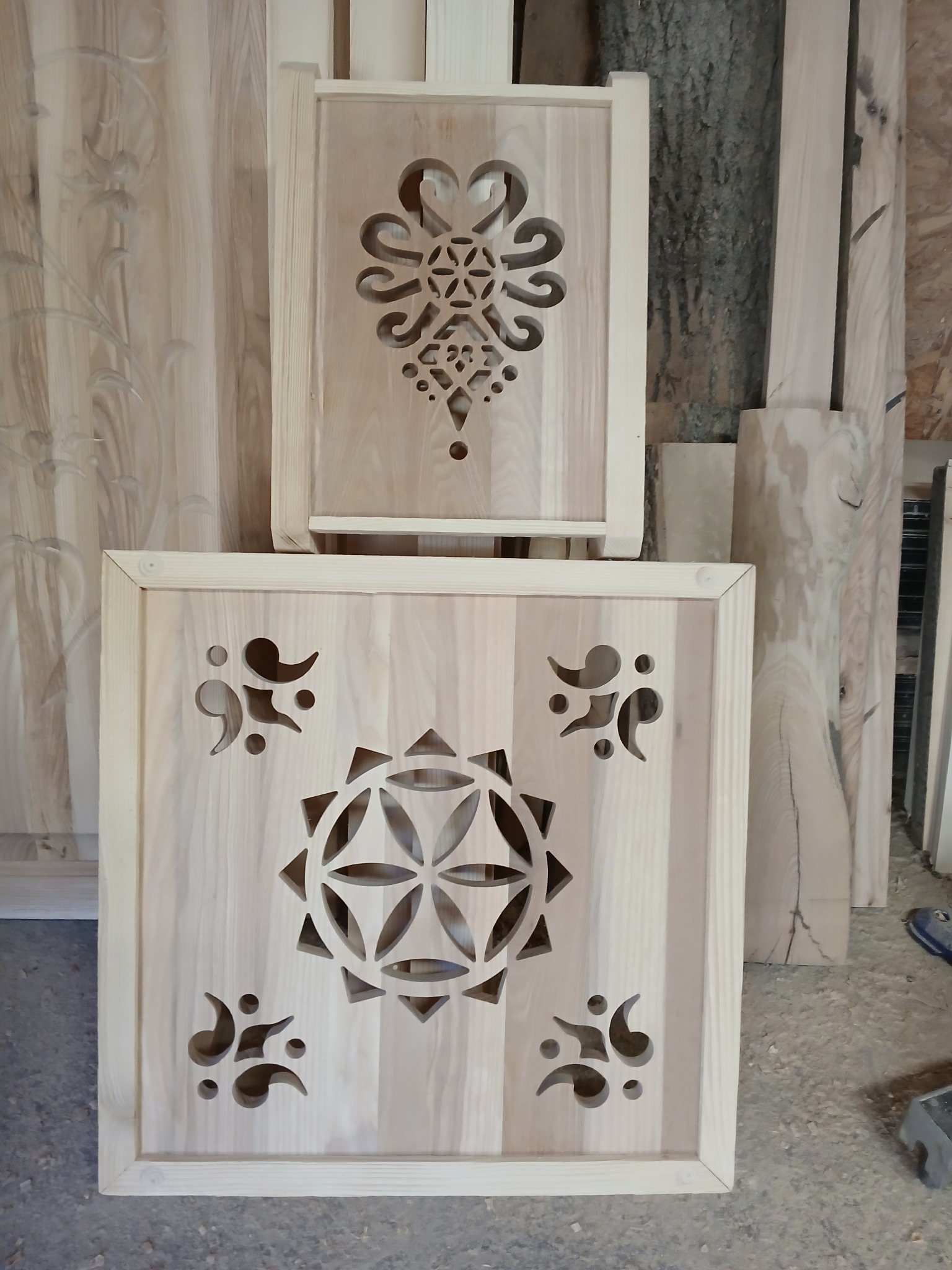 Dwa drewniane panele z wyciętymi laserowo wzorami geometrycznymi i florystycznymi, w jasnym odcieniu drewna. Widoczne fragmenty surowego drewna w tle.