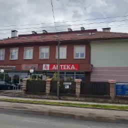 Budynek przychodni w Chełmie z widoczną instalacją zewnętrzną, prawdopodobnie wentylacyjną, na dachu. Na elewacji szyldy informacyjne, w tym apteki i opieki medycznej.