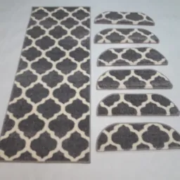 Szary dywanik prostokątny z geometrycznym wzorem i półokrągłe nakładki na schody z takim samym wzorem.