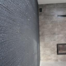 BOHO Bud - Czarna ściana z dekoracyjną fakturą i srebrnymi drobinkami, w tle fragment obudowy kominka z szarych płyt.