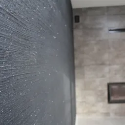 Czarna ściana z dekoracyjną fakturą i srebrnymi drobinkami, w tle fragment obudowy kominka z szarych płyt.