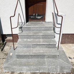Krzysztof Cieślak - Zewnętrzne schody z szarych płytek granitowych z pięcioma stopniami i brązowymi balustradami, prowadzące do drzwi. Na mokrym podłożu obok leży narzędzie.