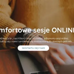 Kobieta w musztardowym swetrze pisze na laptopie, promując komfortowe sesje online, widoczne bransoletki na nadgarstku, ciepłe światło.