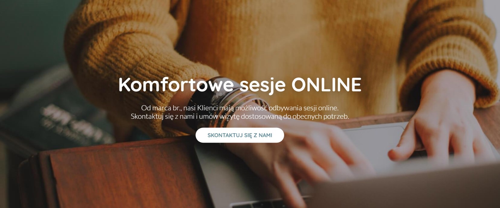 Kobieta w musztardowym swetrze pisze na laptopie, promując komfortowe sesje online, widoczne bransoletki na nadgarstku, ciepłe światło.