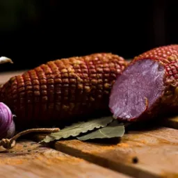 Wędzonka w siatce z czosnkiem i liśćmi laurowymi na desce z widocznymi śladami przypraw.