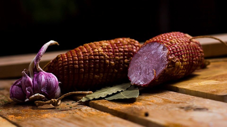 Wędzonka w siatce z czosnkiem i liśćmi laurowymi na desce z widocznymi śladami przypraw.