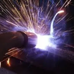 Intensywne iskry podczas łączenia metalowych rur metodą spawania, widoczne ciemne zarysy rur i elektrody.