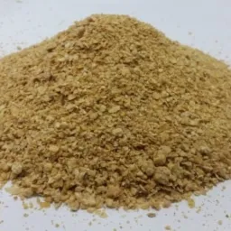 Kopuła jasnobrązowych granulek na białym tle, przypominająca drobny granulat, z widocznymi pojedynczymi cząstkami rozsypanymi wokół podstawy.