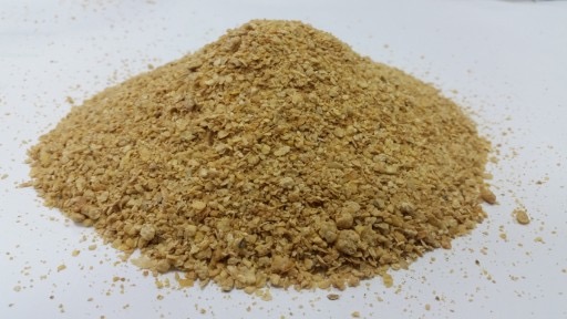 Kopuła jasnobrązowych granulek na białym tle, przypominająca drobny granulat, z widocznymi pojedynczymi cząstkami rozsypanymi wokół podstawy.