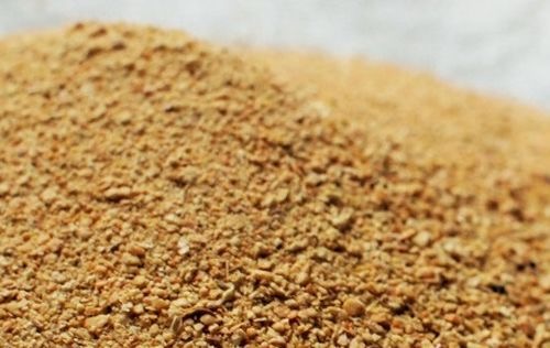 Jasnobrązowa, drobnoziarnista substancja ułożona w kopiec, z widoczną fakturą i nierównościami powierzchni.