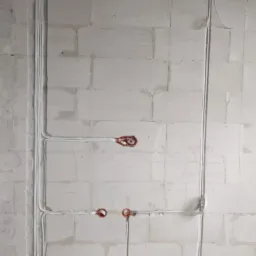 Białe przewody elektryczne ułożone w bruzdach na ścianie z białych pustaków. Widoczne puszki instalacyjne w kolorze czerwonym. Instalacja w trakcie montażu.