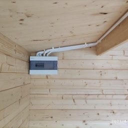 Smart Home Media Mariusz Boruch - Zamknięta skrzynka elektryczna z przewodami na drewnianej ścianie i suficie. Instalacja wewnątrz drewnianego budynku, widok z dołu pod kątem.