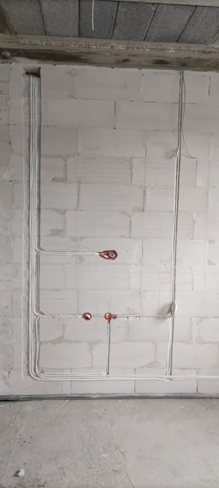 Białe przewody elektryczne ułożone w bruzdach na ścianie z białych pustaków. Widoczne puszki instalacyjne w kolorze czerwonym. Instalacja w trakcie montażu.
