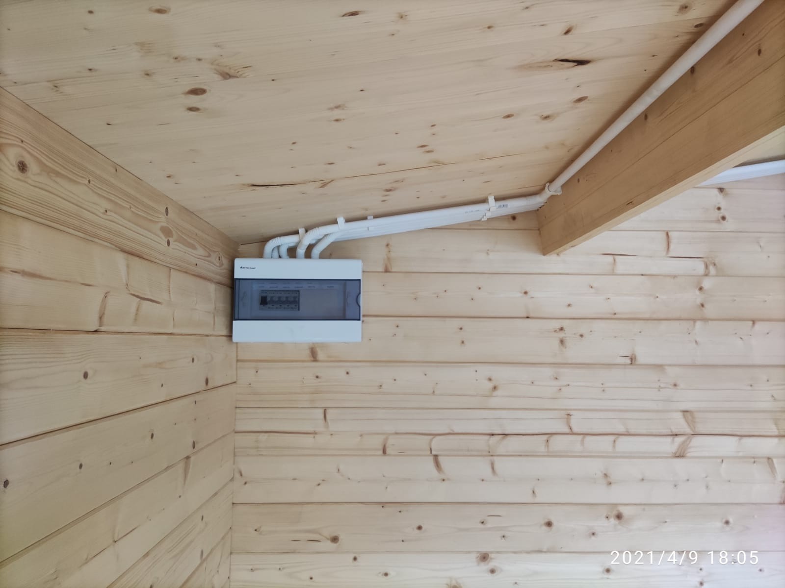 Zamknięta skrzynka elektryczna z przewodami na drewnianej ścianie i suficie. Instalacja wewnątrz drewnianego budynku, widok z dołu pod kątem.
