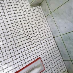 Monika Ibrahim - Białe, kwadratowe płytki mozaikowe na podłodze i ścianach łazienki, widoczna paca do fugowania z resztkami fugi, świeżo po fugowaniu.