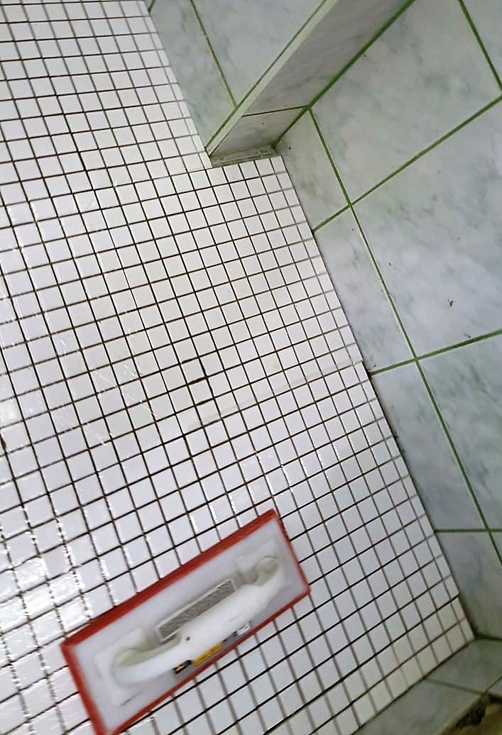 Białe, kwadratowe płytki mozaikowe na podłodze i ścianach łazienki, widoczna paca do fugowania z resztkami fugi, świeżo po fugowaniu.