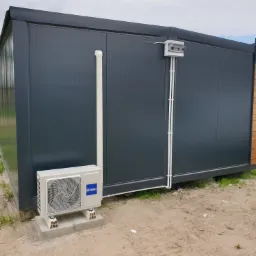 Zewnętrzna jednostka klimatyzacji Haier zamontowana na betonowych bloczkach przy szarym, metalowym kontenerze z widoczną instalacją elektryczną i rurami odprowadzającymi skropliny.