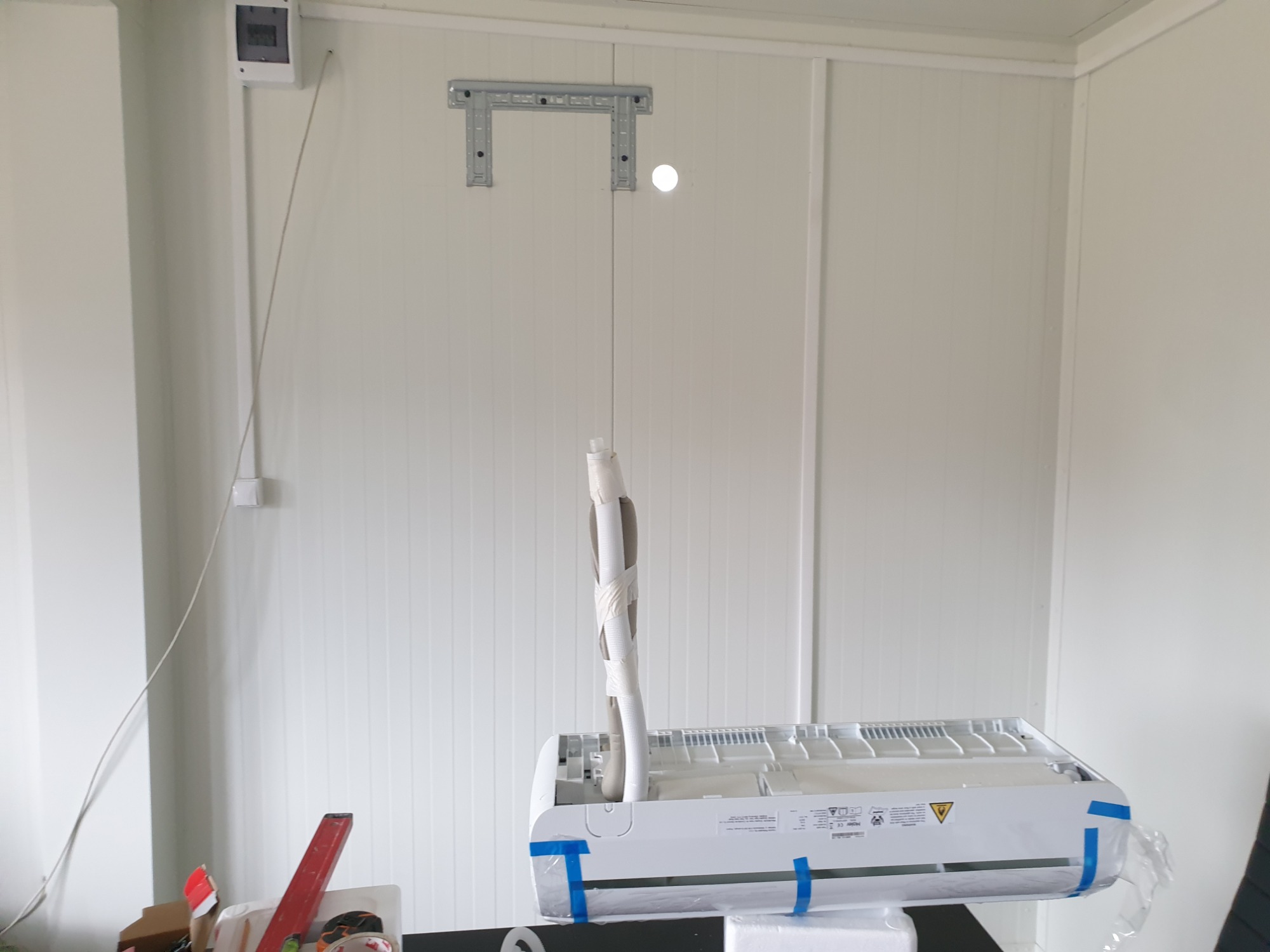 Montaż klimatyzatora: widoczny wewnętrzny moduł jednostki, rury w izolacji owinięte taśmą, zamontowany wspornik na ścianie z paneli, instalacja elektryczna w listwie.