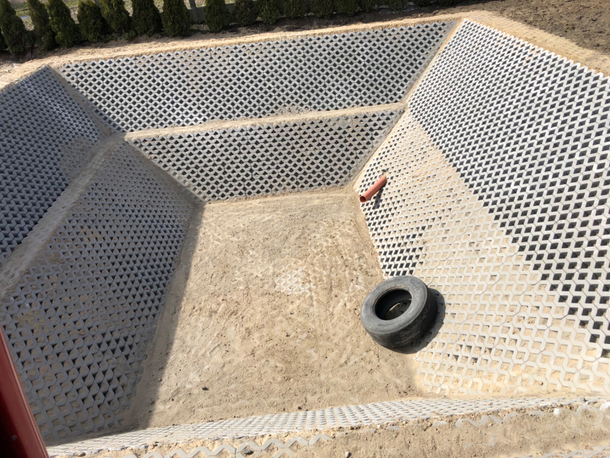 Wykop wyłożony ażurowymi płytami betonowymi, widoczna opona i rura PCV na dnie.