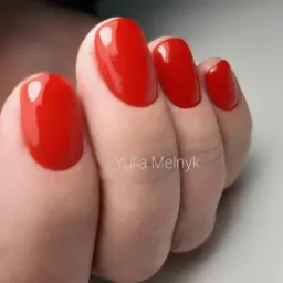 Błyszczące, czerwone paznokcie w kształcie migdała, widoczne z bliska na dłoni z delikatnymi zmarszczkami na skórze.