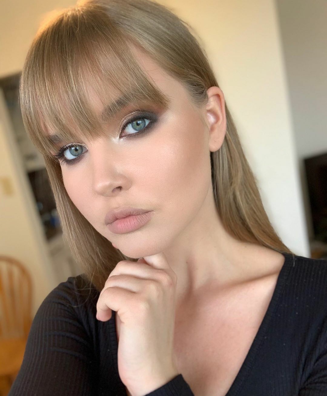 Portret kobiety z blond grzywką i intensywnym smoky eye w odcieniach brązu i szarości, delikatny makijaż ust, dłoń pod brodą.