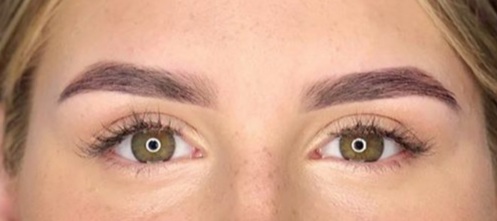 Zbliżenie na kobiece oczy z precyzyjnie wystylizowanymi brwiami w odcieniu ciemnego brązu, podkreślone delikatnym makijażem rzęs.