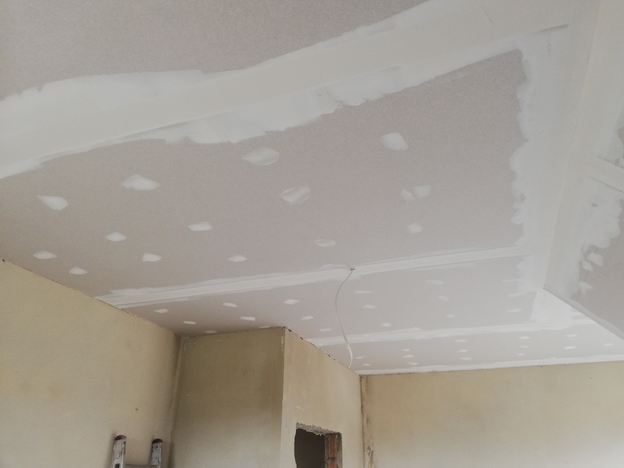 Sufit z płyt karton gips, widoczne łączenia szpachlowane, przygotowane do dalszej obróbki, fragment ściany z widocznym otworem drzwiowym w stanie surowym.