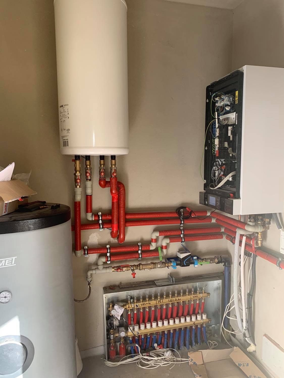 Kotłownia z dwoma zbiornikami, rozdzielaczem podłogówki z licznymi pętlami, oraz piecem z otwartą obudową ukazującą wewnętrzne komponenty.