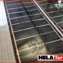 Rozłożona mata grzewcza podłogowa z widocznymi elementami grzejnymi i folią izolacyjną w kratkę, z logo producenta Hela Term w prawym dolnym rogu.