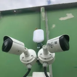 Dwie kamery monitoringu marki Dahua zamontowane na zielonej ścianie budynku, z widocznym białym modułem komunikacyjnym i przewodami w peszlach.