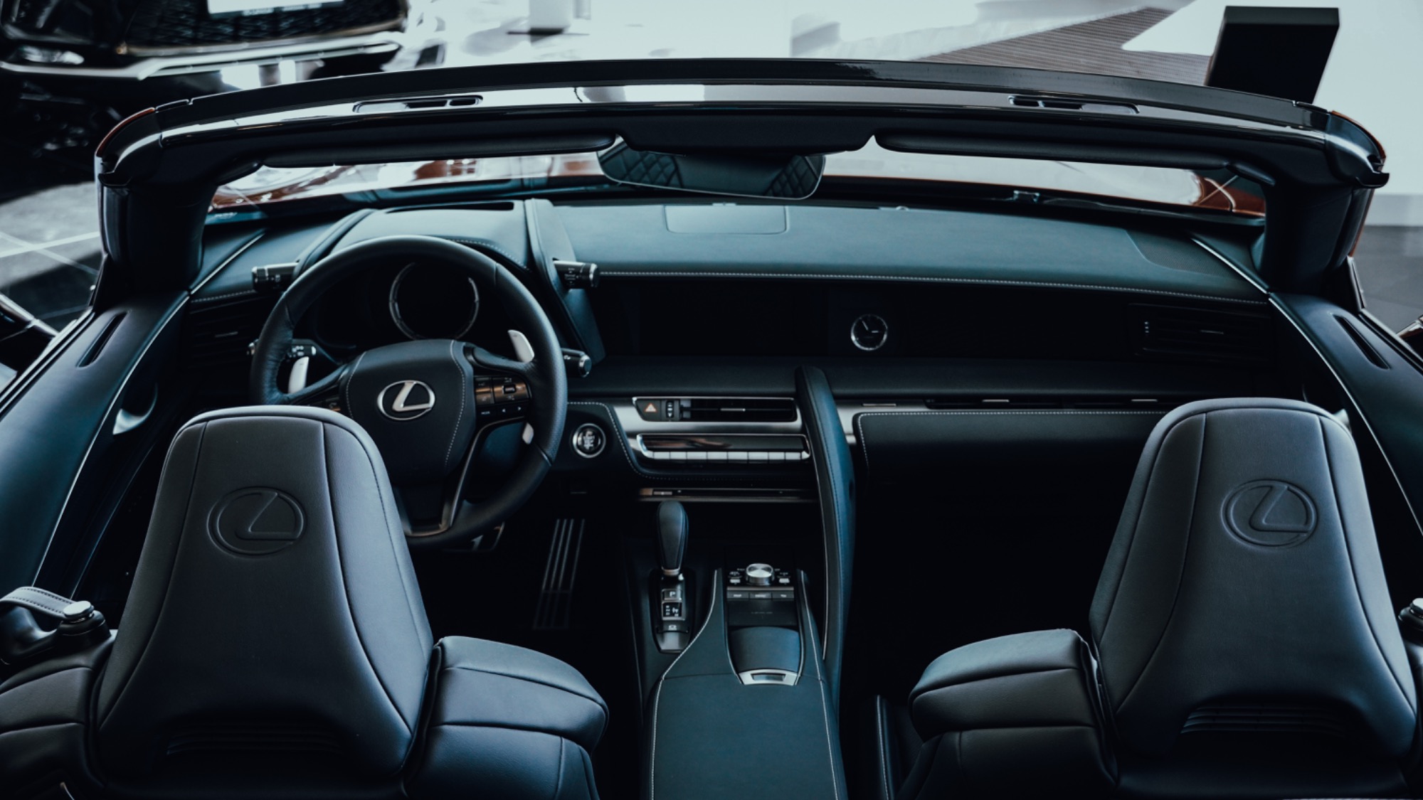 Wnętrze luksusowego kabrioletu Lexus LC z czarną skórzaną tapicerką, widok z tylnych siedzeń na deskę rozdzielczą i kierownicę z logo, eleganckie wykończenie.