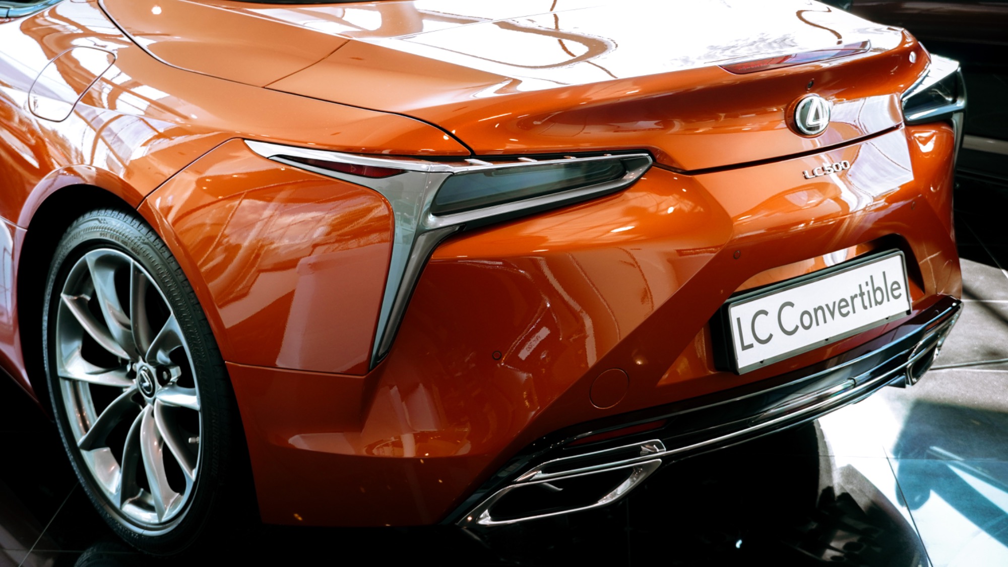 Pomarańczowy Lexus LC 500 Convertible, widok z tyłu, z chromowanymi detalami i felgami, zaparkowany na błyszczącej powierzchni.