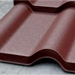Brązowa dachówka metalowa o falistym profilu, widoczna z bliska na szarym tle. Teksturowana powierzchnia, imitująca tradycyjną dachówkę ceramiczną.