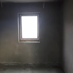 Surowe wnętrze z oknem OknoPlast przed wykończeniem, ściany pokryte świeżym, szarym tynkiem, widoczne przewody elektryczne pod sufitem.