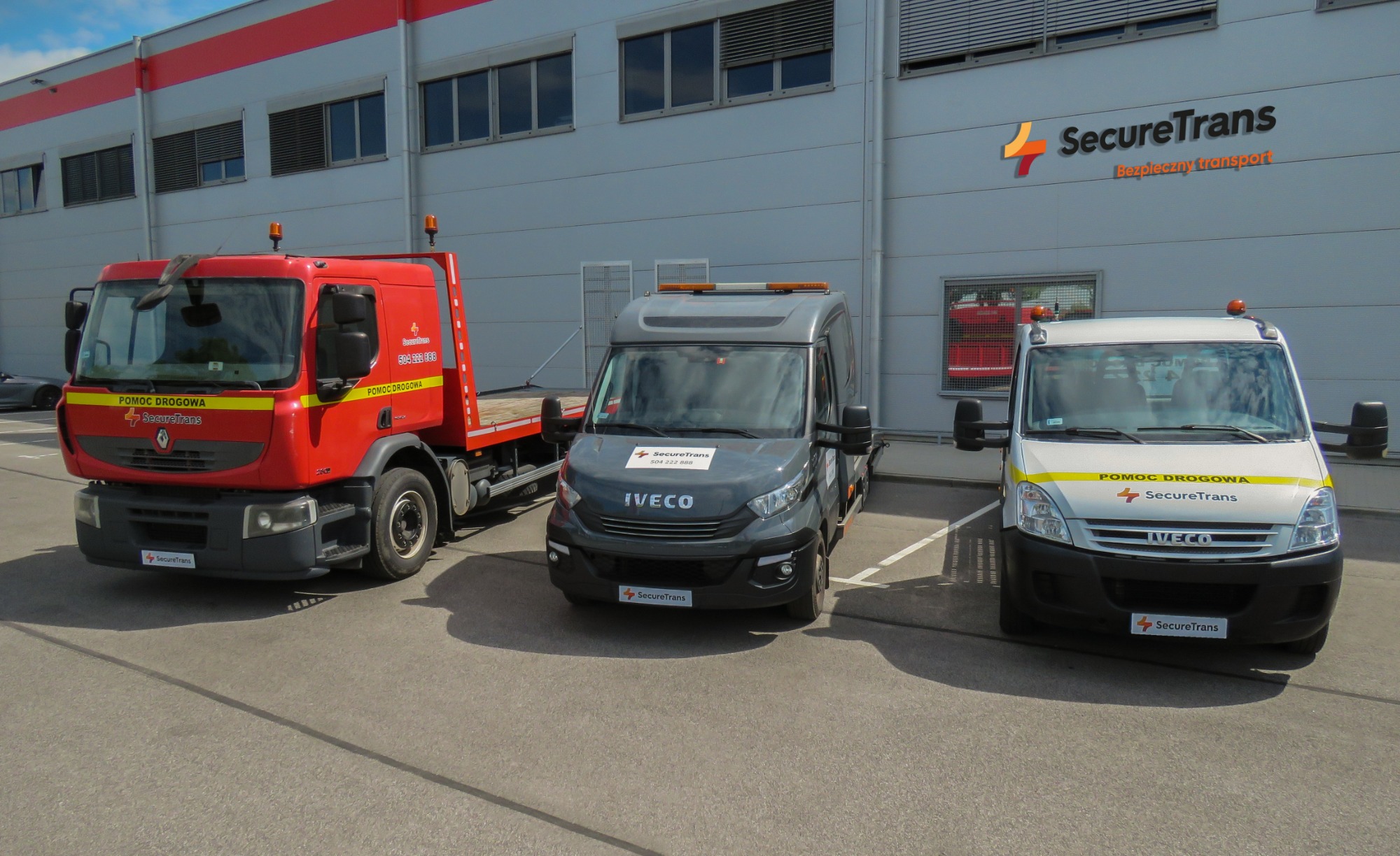 Flota firmy SecureTrans: czerwona laweta Renault, szary i biały bus Iveco, wszystkie pojazdy zaparkowane przed budynkiem z logo firmy.