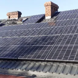 Panele słoneczne na dachu z dachówką ceramiczną i kominami z cegły w słoneczny dzień.