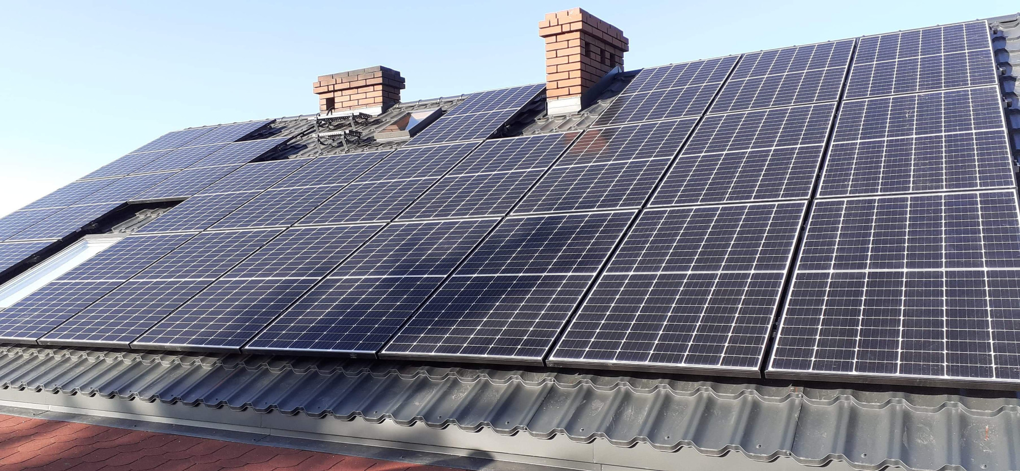 Panele słoneczne na dachu z dachówką ceramiczną i kominami z cegły w słoneczny dzień.