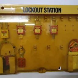 Żółta stacja blokad Lockout Station z różnymi zamkami i zawieszkami ostrzegawczymi, w tym zamki z napisem 'DANGER LOCKED OUT DO NOT REMOVE' oraz zawieszka 'UWAGA STOP'.