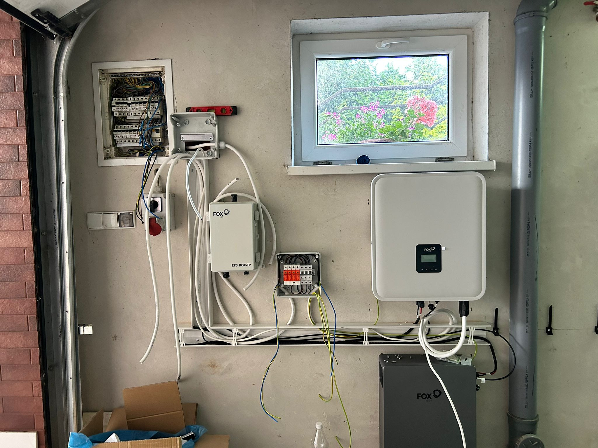 Instalacja elektryczna z elementami systemu fotowoltaicznego w garażu: rozdzielnica, zabezpieczenia EPS BOX-TP, inwerter z wyświetlaczem i akumulator energii firmy FOX ESS, widoczne okablowanie...