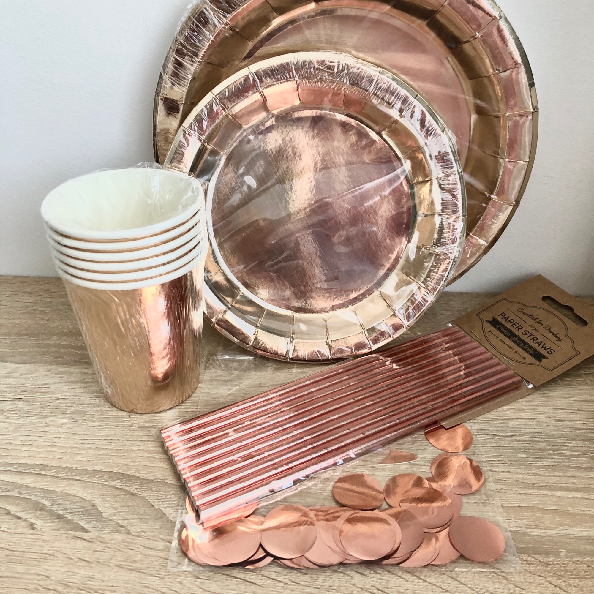 Zestaw imprezowy w kolorze różowego złota: talerze papierowe, kubeczki, słomki i konfetti w folii, gotowe na przyjęcie.