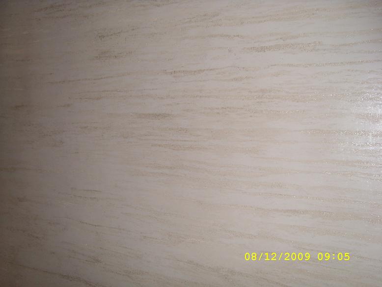 Beżowa ściana pokryta tynkiem akrylowym o strukturze kornika z ziarnem 1.5:2.0:2.5, widoczne delikatne, poziome smugi.