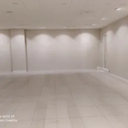 Puste pomieszczenie z beżowymi ścianami, kwadratową podłogą z płytek i oświetleniem sufitowym, przygotowane do dalszych prac wykończeniowych.