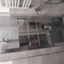 Szklana kabina prysznicowa z widocznym zestawem prysznicowym, grzejnikiem drabinkowym i akcesoriami łazienkowymi na tle płytek w odcieniach szarości, z elementami wyposażenia, takimi jak ręcznik...